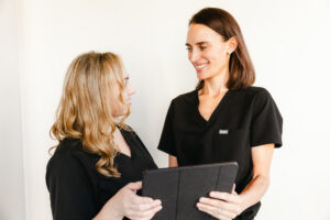 A provider in a black uniform holds an iPad and smiles with another provider about liposuction near Brentwood, TN.
