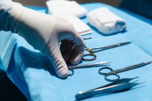 A close-up of a surgeon wearing plastic gloves grabbing a pair of scissors from a set of tools for ab abdominoplasty in Nashville.